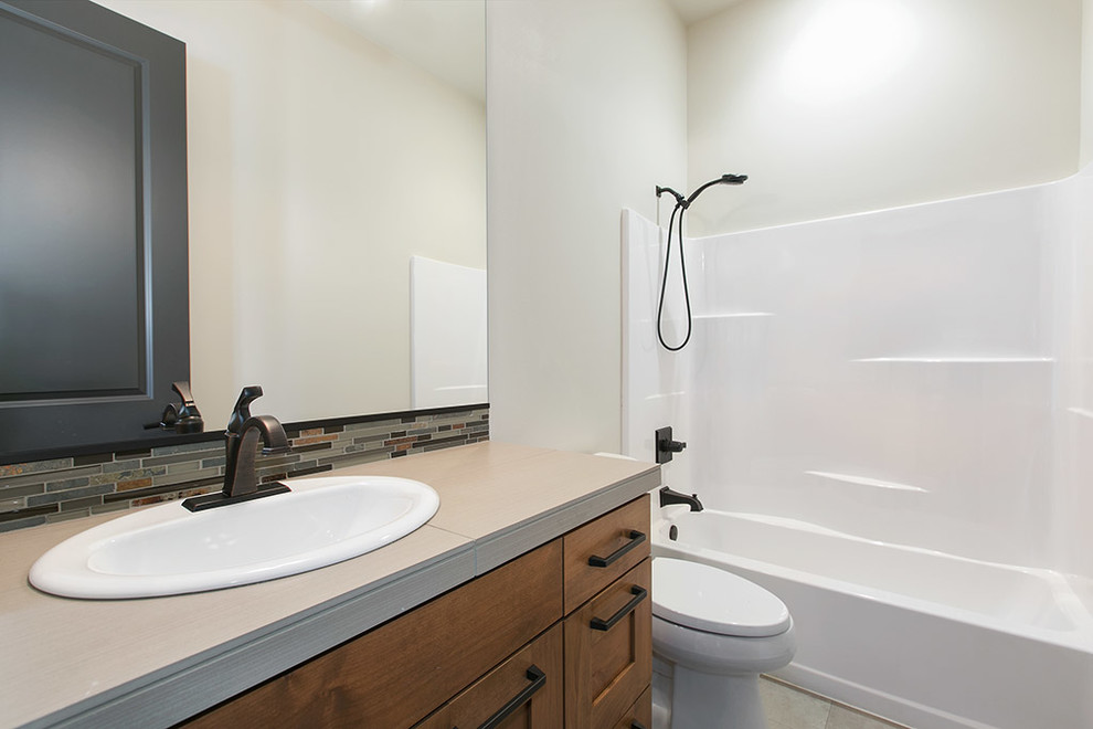 Cette image montre une petite salle de bain chalet en bois brun pour enfant avec un lavabo posé, un plan de toilette en carrelage, une baignoire posée, un combiné douche/baignoire, WC séparés, un carrelage gris, des carreaux de porcelaine et un mur gris.