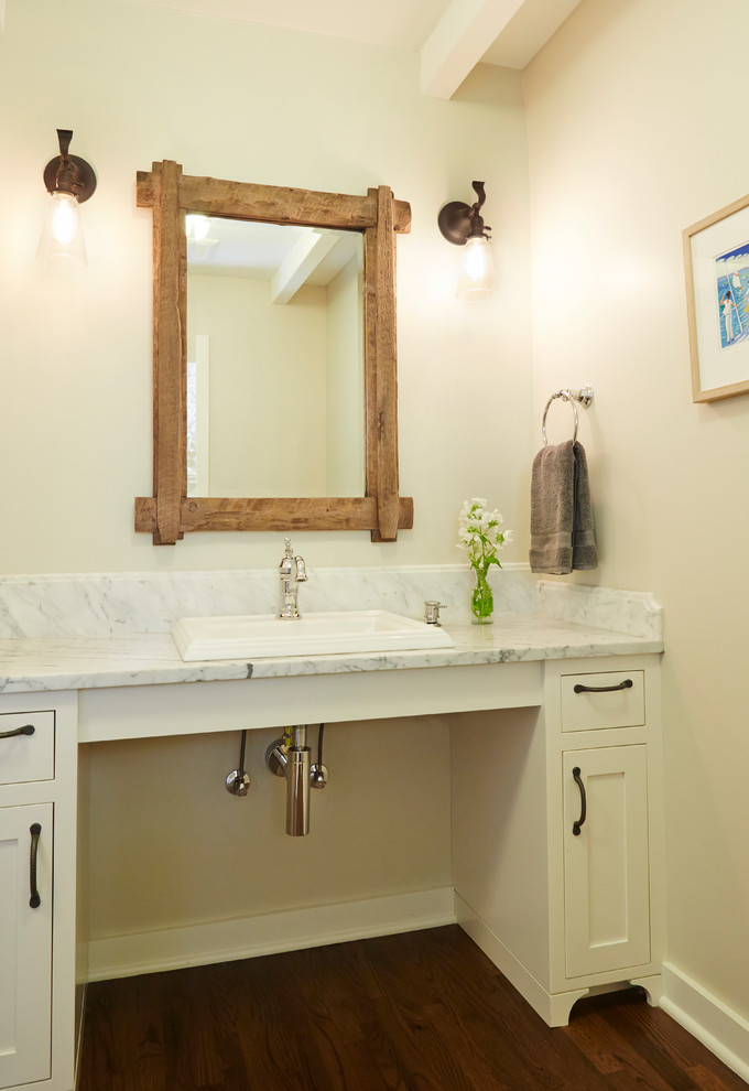 Foto på ett mellanstort vintage badrum, med ett nedsänkt handfat, vita skåp, marmorbänkskiva, beige väggar, mörkt trägolv och skåp i shakerstil