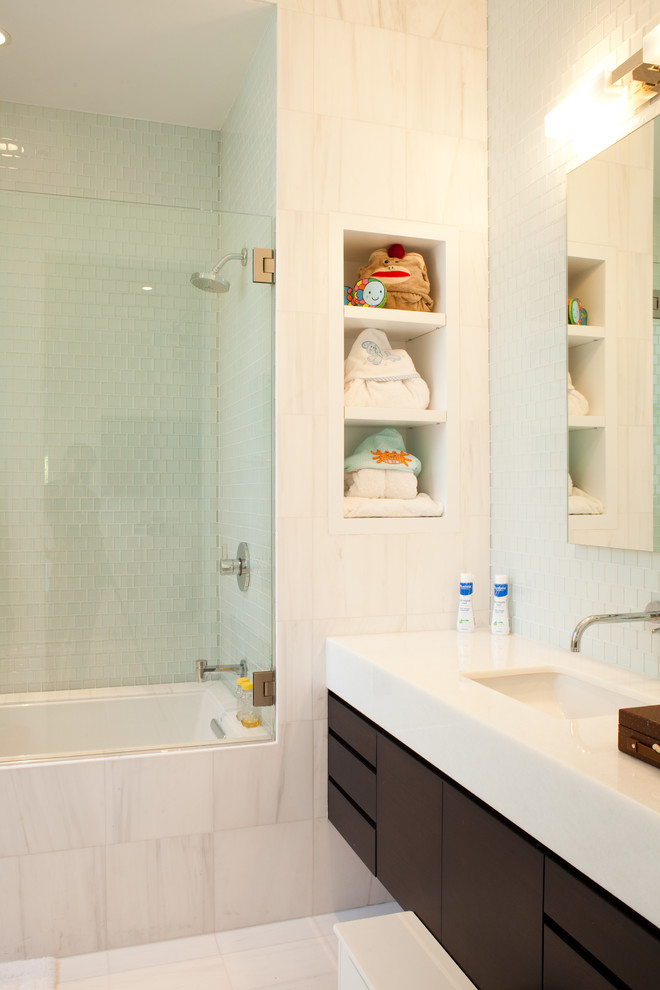 Idée de décoration pour une salle de bain design en bois foncé avec un lavabo encastré, un placard à porte plane, une baignoire encastrée, un combiné douche/baignoire et un carrelage blanc.