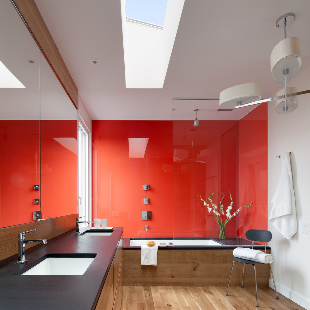Idée de décoration pour une salle de bain design en bois clair avec un lavabo encastré, un placard à porte plane, un plan de toilette en stéatite, une baignoire encastrée, un combiné douche/baignoire, des plaques de verre, un mur blanc, parquet clair et un carrelage rouge.