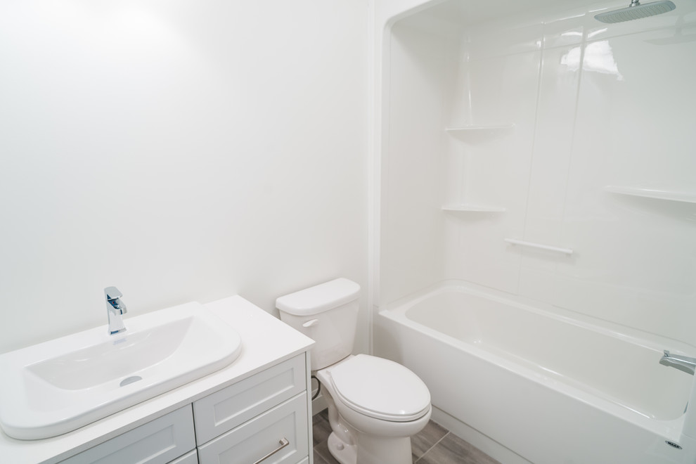 Imagen de cuarto de baño rural de tamaño medio con armarios estilo shaker, puertas de armario blancas, bañera empotrada, combinación de ducha y bañera, sanitario de una pieza, paredes blancas, lavabo encastrado, suelo gris y ducha abierta
