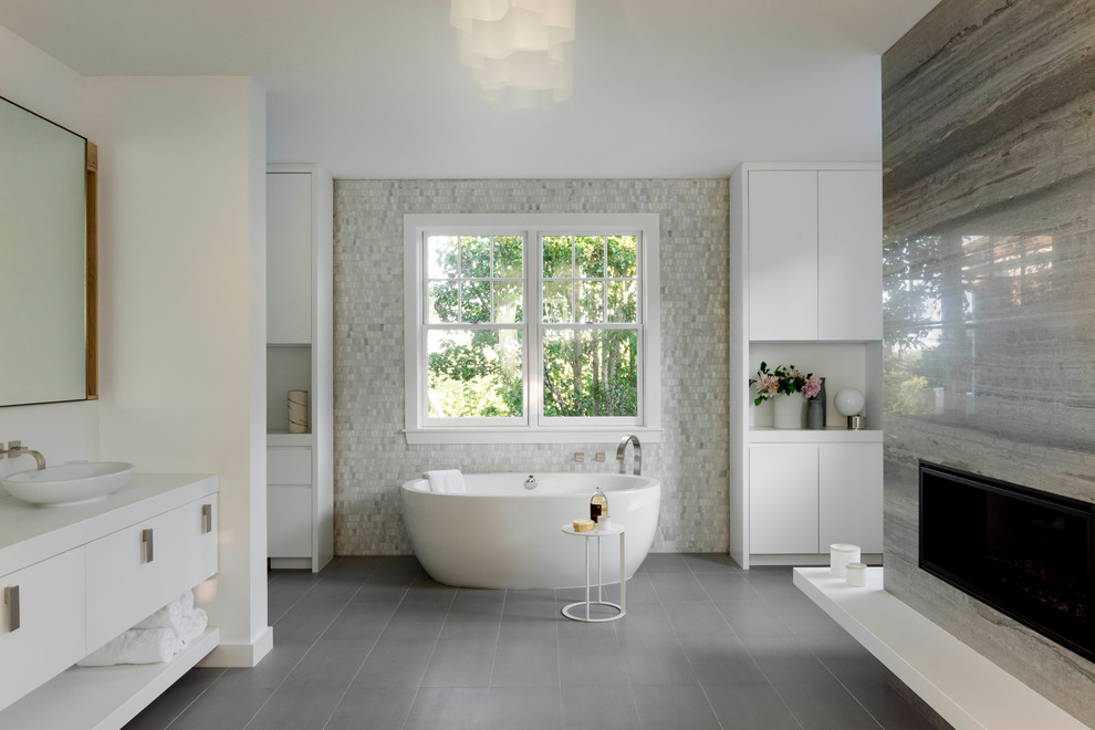 Cette image montre une salle de bain design avec un placard à porte plane, des portes de placard blanches, une baignoire indépendante, un carrelage gris, un carrelage blanc, mosaïque, un mur blanc, une vasque, un sol gris et un plan de toilette blanc.