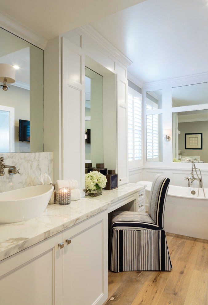 Exempel på ett stort maritimt en-suite badrum, med luckor med infälld panel, vita skåp, ett fristående badkar, vit kakel, stenhäll, vita väggar, ljust trägolv, ett fristående handfat och marmorbänkskiva