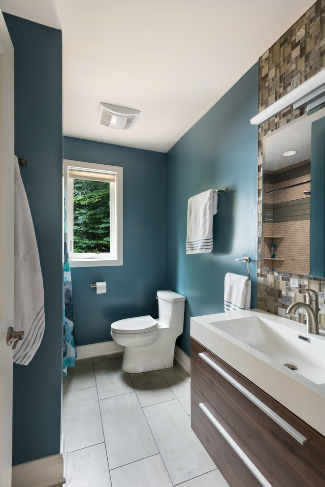 Example of a mid-sized 1960s 3/4 gray tile and glass tile ceramic tile and gray floor bathroom design in Baltimore with a one-piece toilet, dark wood cabinets, blue walls, flat-panel cabinets, a console sink and solid surface countertops