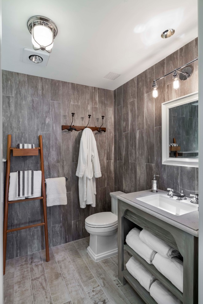 Inredning av ett mellanstort badrum, med öppna hyllor, skåp i slitet trä, ett hörnbadkar, grå kakel, porslinskakel, klinkergolv i porslin, ett konsol handfat, marmorbänkskiva och grått golv