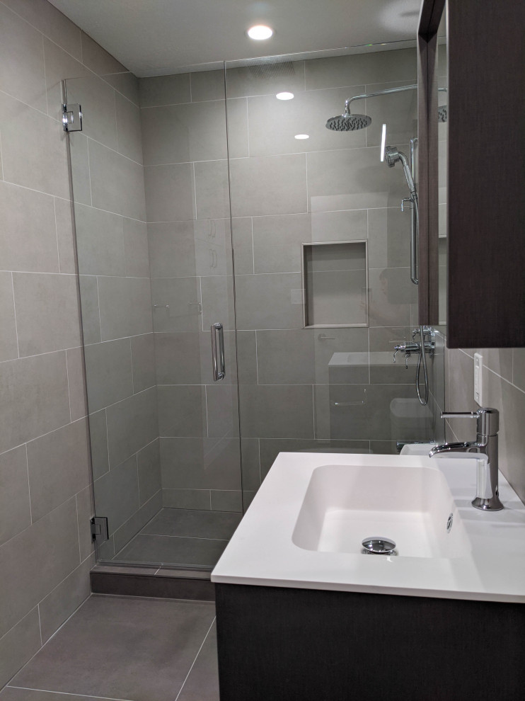 Inredning av ett modernt mellanstort vit vitt badrum med dusch, med släta luckor, bruna skåp, en dusch i en alkov, en toalettstol med separat cisternkåpa, grå kakel, porslinskakel, grå väggar, klinkergolv i porslin, ett integrerad handfat, bänkskiva i akrylsten, grått golv och dusch med gångjärnsdörr