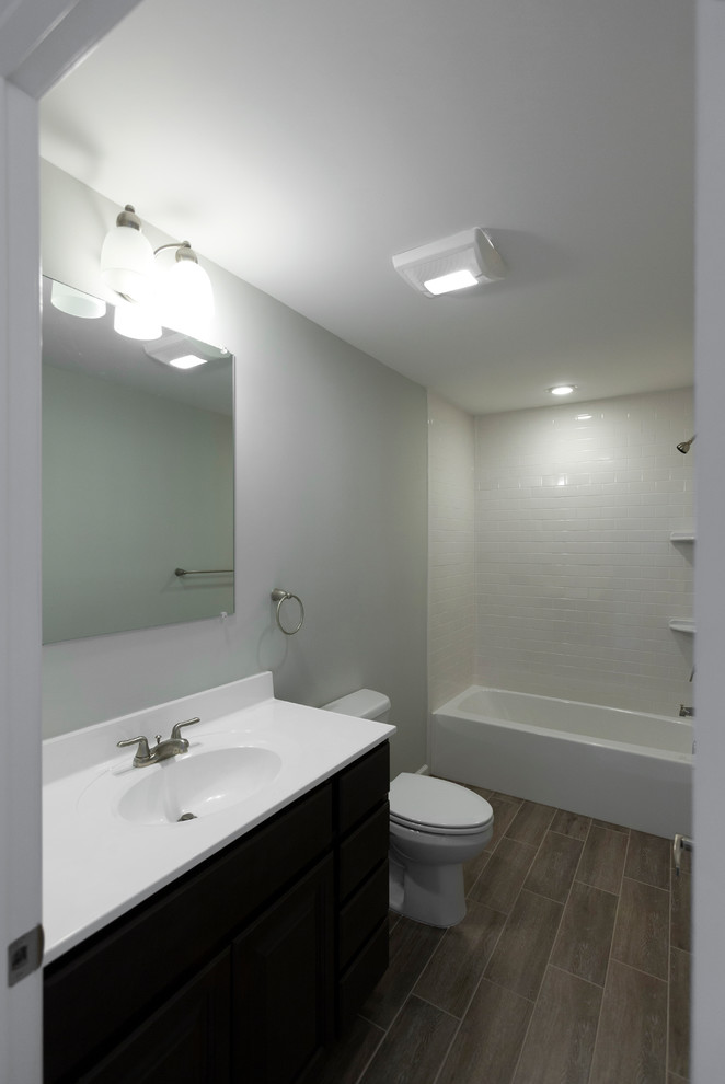 Klassisk inredning av ett mellanstort badrum med dusch, med släta luckor, svarta skåp, ett badkar i en alkov, en dusch/badkar-kombination, en toalettstol med separat cisternkåpa, vit kakel, tunnelbanekakel, grå väggar, mörkt trägolv, ett integrerad handfat, bänkskiva i kvarts och brunt golv