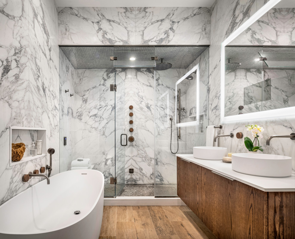 Inspiration for a contemporary ensuite bathroom in New York with flat-panel cabinets, a freestanding bath, porcelain tiles, a hinged door, white worktops, double sinks, a floating vanity unit, an alcove shower, wood-effect flooring, a vessel sink and brown floors.