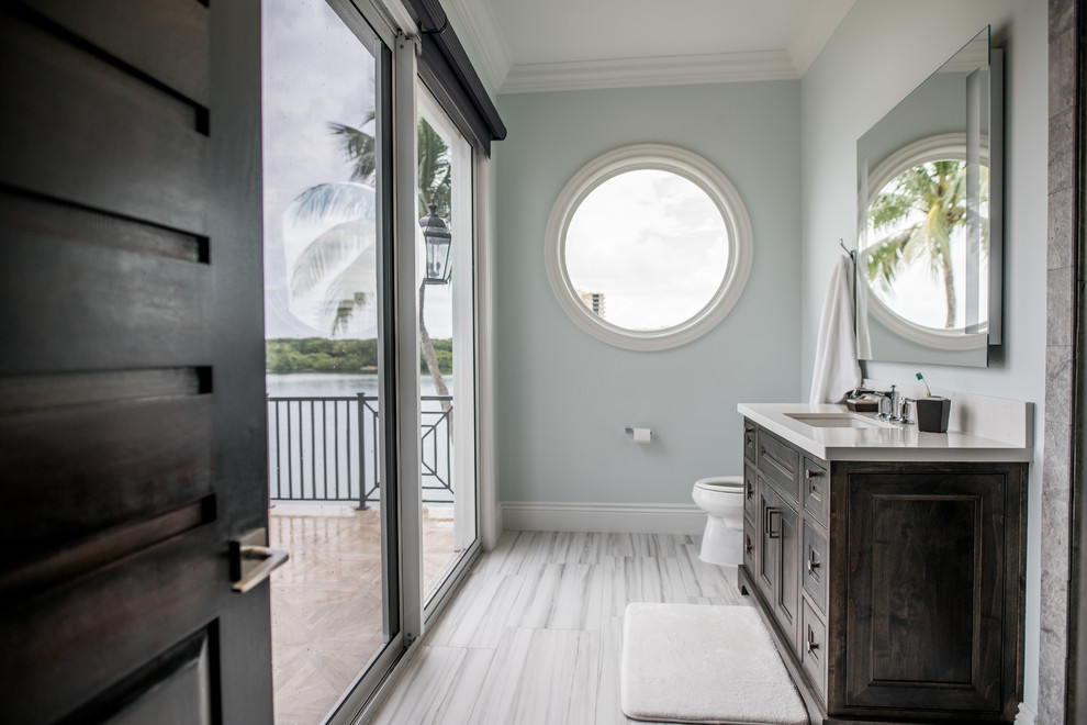 Inspiration for a medium sized contemporary shower room bathroom in Miami with recessed-panel cabinets, dark wood cabinets, a one-piece toilet, blue walls, porcelain flooring, a submerged sink and solid surface worktops.