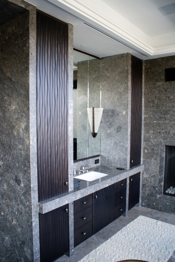 Cette photo montre une grande salle de bain principale tendance avec un placard à porte persienne, des portes de placard noires, une baignoire indépendante, un carrelage noir, un carrelage gris, des carreaux de porcelaine, un mur gris, un sol en carrelage de porcelaine, un lavabo encastré et un plan de toilette en granite.