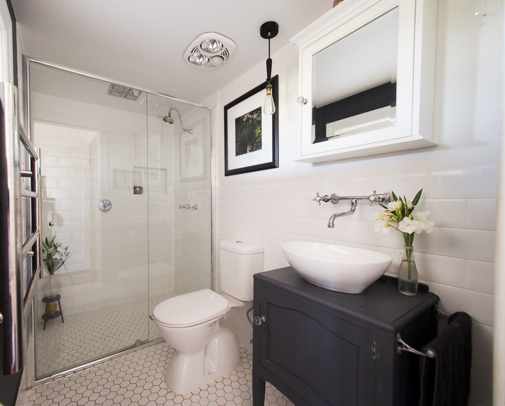 Inredning av ett klassiskt litet badrum med dusch, med möbel-liknande, grå skåp, en kantlös dusch, en toalettstol med hel cisternkåpa, vit kakel, porslinskakel, vita väggar, mosaikgolv, ett fristående handfat och träbänkskiva