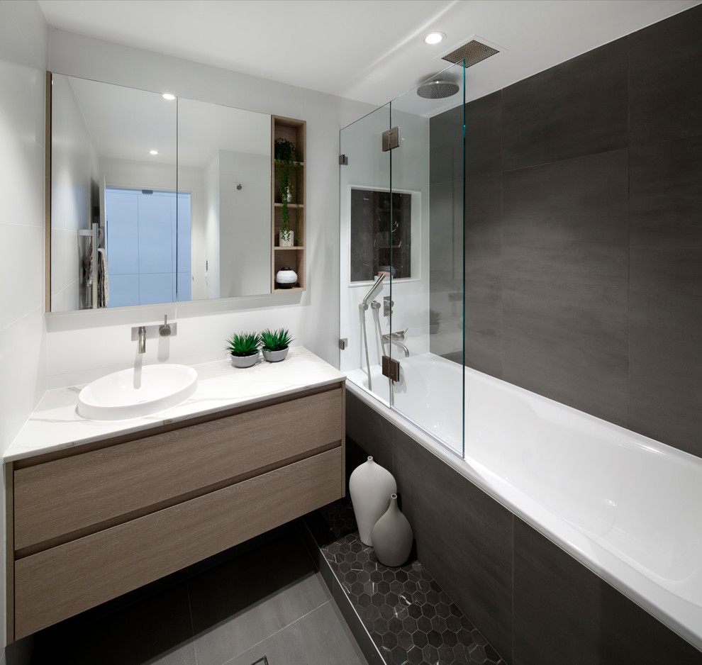 Exemple d'une salle d'eau moderne en bois clair de taille moyenne avec un placard à porte plane, une douche ouverte, WC suspendus, un carrelage gris, des carreaux de porcelaine, un mur gris, un sol en carrelage de porcelaine, un lavabo posé, un plan de toilette en quartz modifié, un sol gris, aucune cabine et un plan de toilette blanc.