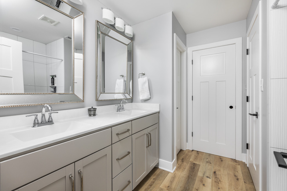 Imagen de cuarto de baño principal marinero de tamaño medio con armarios estilo shaker, puertas de armario grises, paredes grises, suelo de madera clara y encimeras blancas
