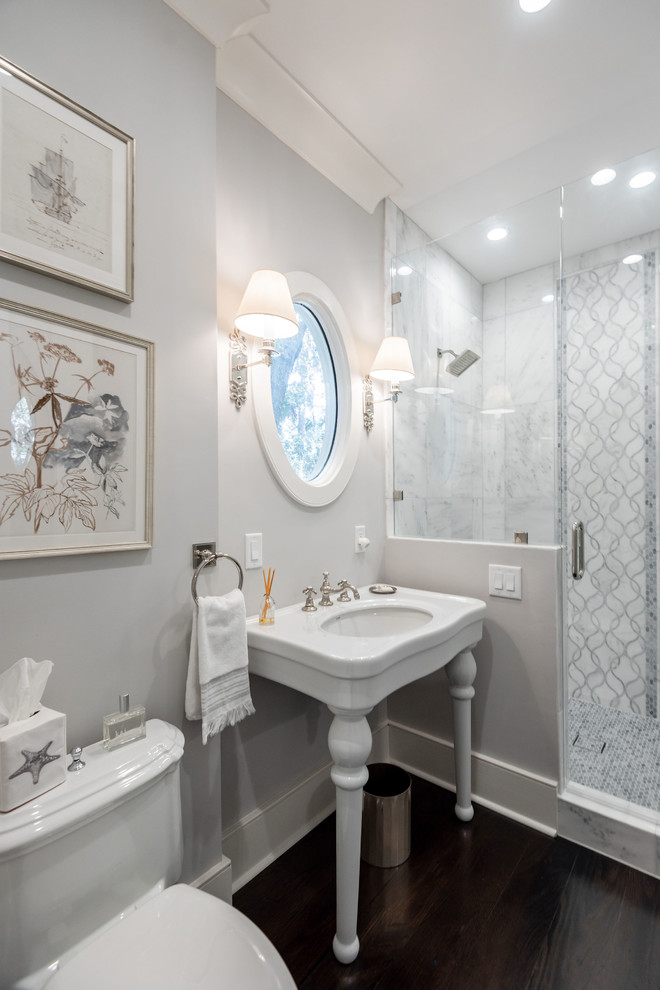 Foto på ett litet vintage badrum, med en toalettstol med hel cisternkåpa, grå kakel, vit kakel, grå väggar, mörkt trägolv, ett piedestal handfat, brunt golv, dusch med gångjärnsdörr och en dusch i en alkov