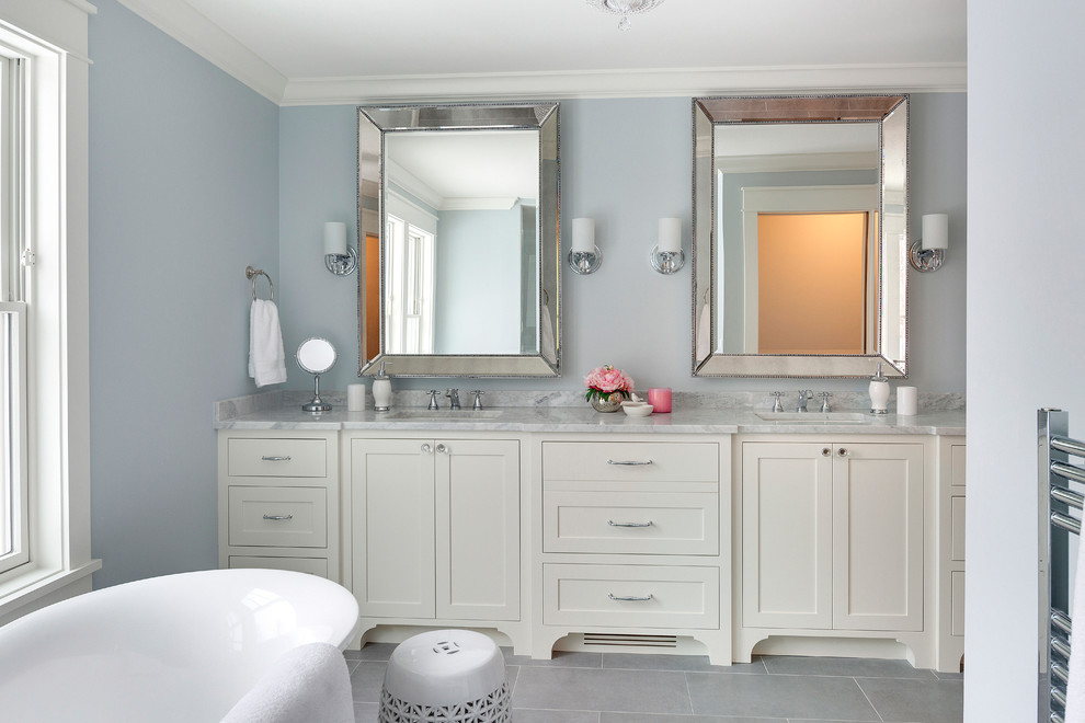 Réalisation d'une salle de bain principale tradition avec un placard à porte shaker, des portes de placard blanches, une baignoire indépendante, un carrelage gris, un mur bleu, un sol en carrelage de céramique et un plan de toilette en marbre.