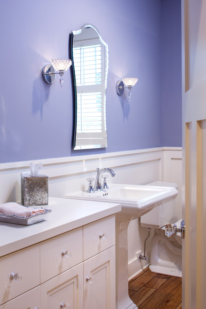 Example of a mid-sized classic medium tone wood floor bathroom design in Minneapolis with a pedestal sink, recessed-panel cabinets, white cabinets, wood countertops and purple walls