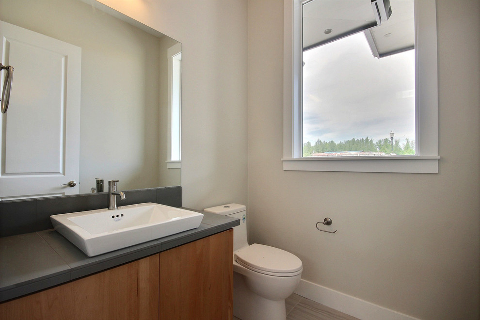 Exemple d'une salle d'eau moderne en bois brun de taille moyenne avec un placard à porte plane, WC séparés, un carrelage gris, des carreaux de porcelaine, un mur beige, un sol en carrelage de céramique, une vasque, un plan de toilette en carrelage, un sol gris et un plan de toilette gris.