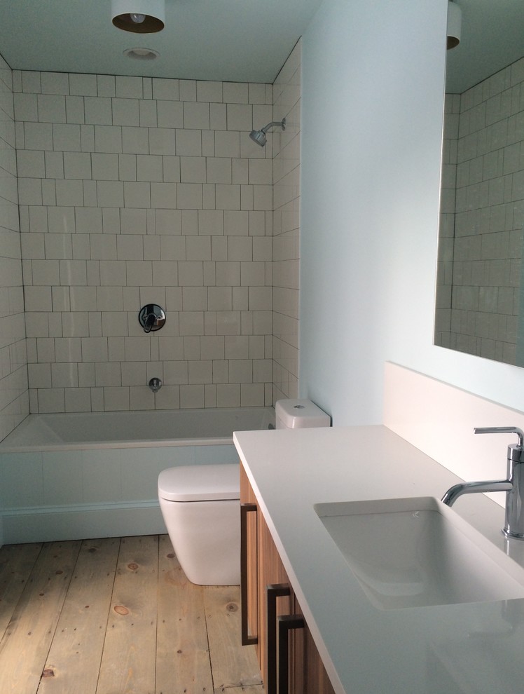 Medium sized scandi family bathroom in New York with freestanding cabinets, medium wood cabinets, an alcove bath, a shower/bath combination, a one-piece toilet, white tiles, ceramic tiles, white walls, light hardwood flooring, a submerged sink and solid surface worktops.