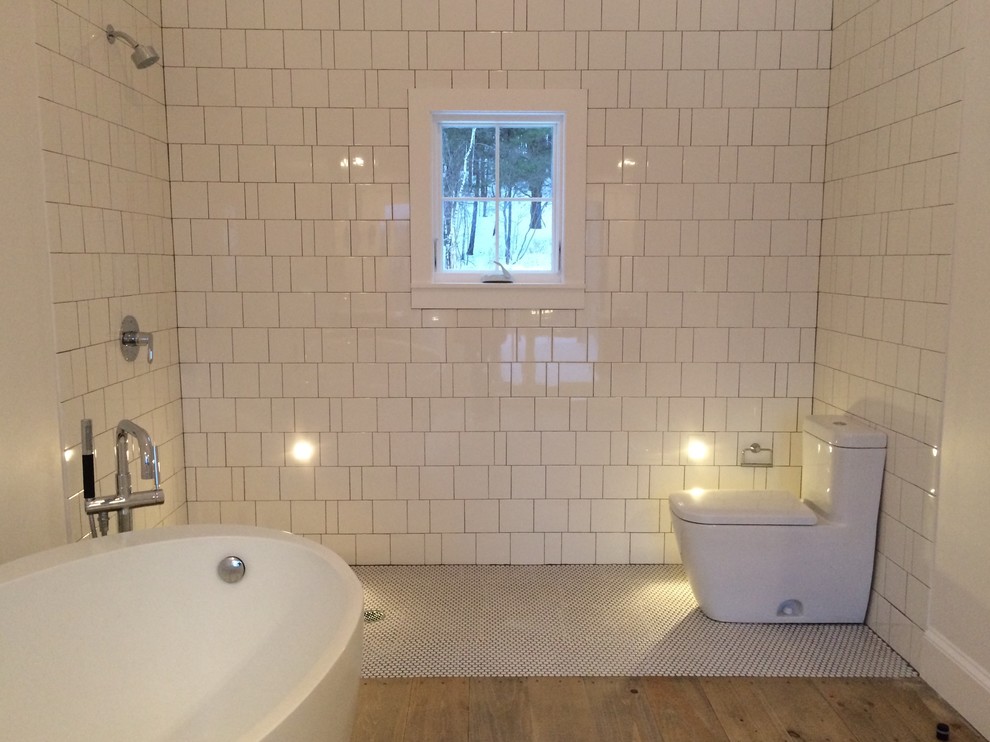 Large scandi ensuite wet room bathroom in New York with a freestanding bath, a one-piece toilet, white tiles, ceramic tiles, white walls, light hardwood flooring, an open shower, freestanding cabinets, medium wood cabinets, a submerged sink and solid surface worktops.