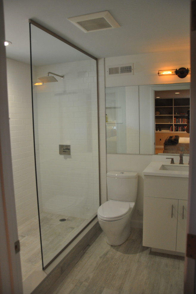Mid-sized urban 3/4 porcelain tile and white tile porcelain tile alcove shower photo in New York with flat-panel cabinets, white cabinets, a two-piece toilet, white walls, solid surface countertops and an integrated sink