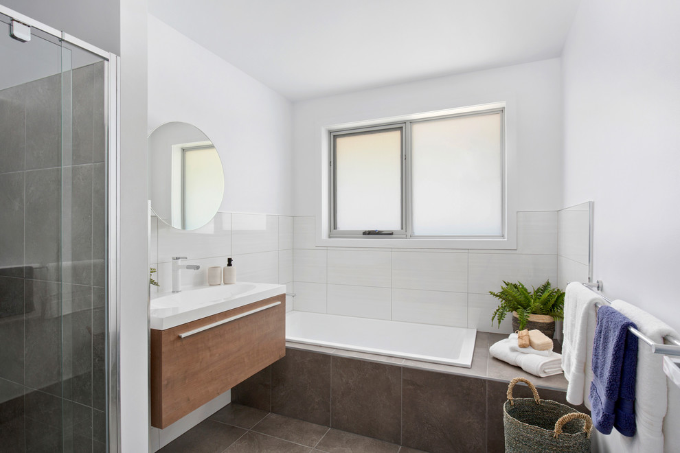 На фото: маленькая главная ванная комната в современном стиле с фасадами с декоративным кантом, светлыми деревянными фасадами, накладной ванной, душем в нише, унитазом-моноблоком, белой плиткой, белыми стенами, полом из керамической плитки, подвесной раковиной, столешницей из искусственного камня, коричневым полом, душем с распашными дверями и белой столешницей для на участке и в саду