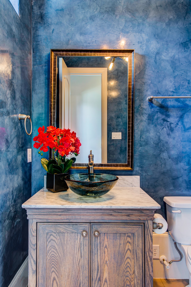 Cette image montre un petit WC et toilettes design en bois brun avec un placard avec porte à panneau encastré, WC séparés, un mur bleu, un sol en bois brun, une vasque, un plan de toilette en marbre et un sol marron.