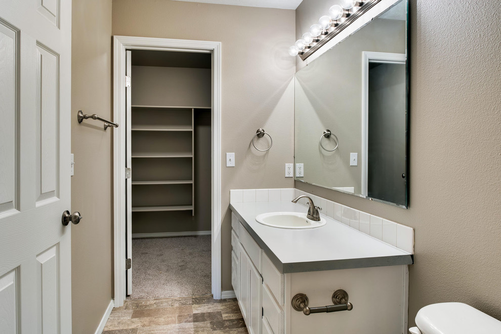 Klassisk inredning av ett litet en-suite badrum, med luckor med upphöjd panel, vita skåp, ett badkar i en alkov, en dusch/badkar-kombination, en toalettstol med separat cisternkåpa, vit kakel, porslinskakel, beige väggar, vinylgolv, ett nedsänkt handfat och laminatbänkskiva