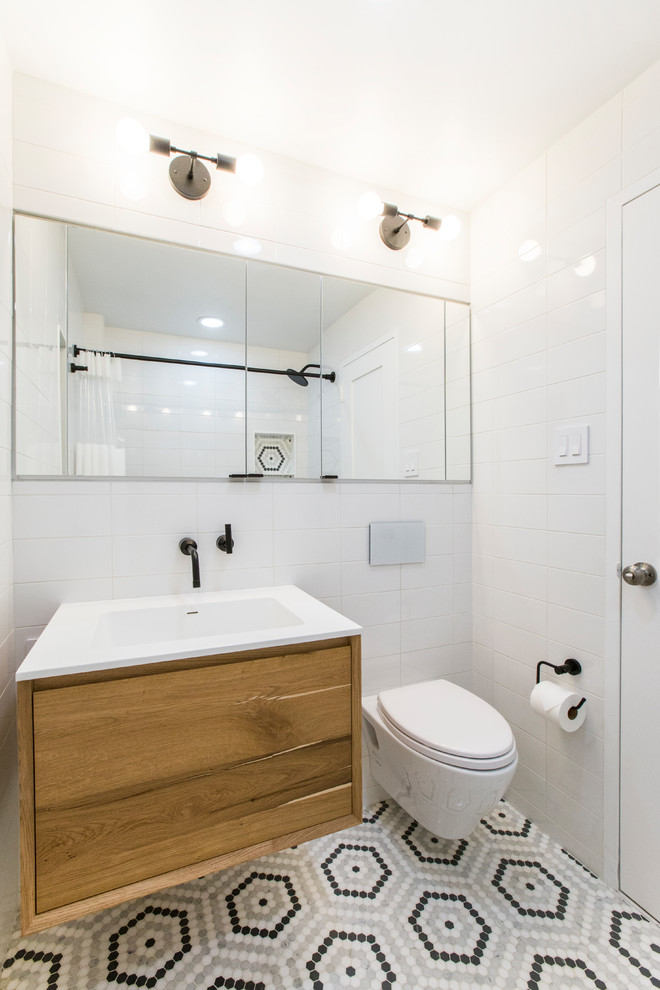 ニューヨークにあるお手頃価格の中くらいなコンテンポラリースタイルのおしゃれなマスターバスルーム (フラットパネル扉のキャビネット、中間色木目調キャビネット、アルコーブ型浴槽、シャワー付き浴槽	、壁掛け式トイレ、白いタイル、磁器タイル、白い壁、大理石の床、壁付け型シンク、人工大理石カウンター、マルチカラーの床、シャワーカーテン、白い洗面カウンター) の写真