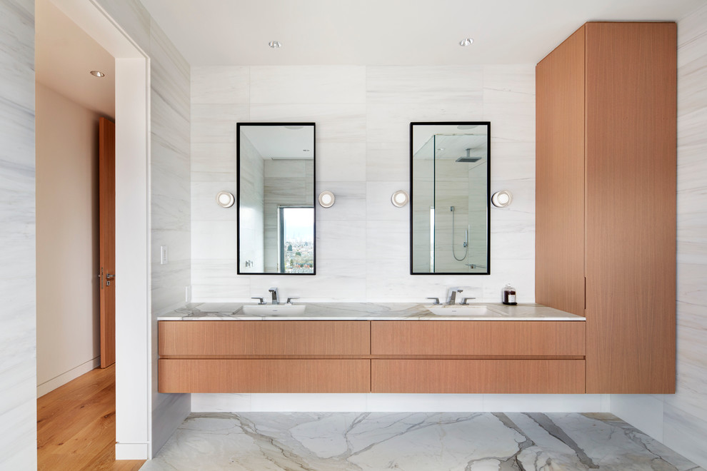 This is an example of a large contemporary ensuite bathroom in Vancouver with flat-panel cabinets, light wood cabinets, a freestanding bath, a corner shower, a one-piece toilet, white tiles, stone tiles, white walls, marble flooring, a submerged sink and marble worktops.