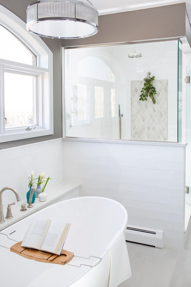 На фото: огромная главная ванная комната в стиле неоклассика (современная классика) с фасадами в стиле шейкер, белыми фасадами, отдельно стоящей ванной, угловым душем, унитазом-моноблоком, белой плиткой, керамической плиткой, серыми стенами, полом из керамогранита, врезной раковиной, столешницей из искусственного кварца, серым полом, душем с распашными дверями и белой столешницей с