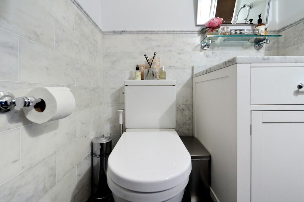 Inredning av ett modernt litet badrum, med ett integrerad handfat, luckor med upphöjd panel, vita skåp, marmorbänkskiva, en toalettstol med separat cisternkåpa, vit kakel, grå väggar och mörkt trägolv