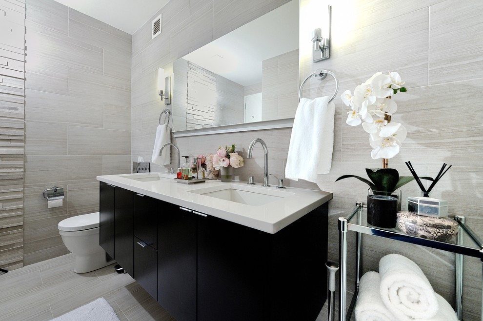 Exemple d'une salle de bain tendance de taille moyenne avec un lavabo intégré, un placard à porte plane, des portes de placard noires, un plan de toilette en surface solide, une baignoire en alcôve, un combiné douche/baignoire, WC séparés, un carrelage gris et un mur beige.