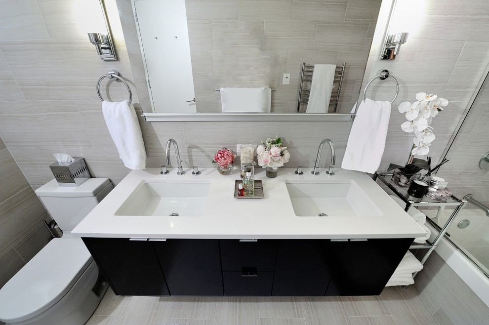 Inspiration for a medium sized contemporary bathroom in New York with an integrated sink, flat-panel cabinets, black cabinets, solid surface worktops, an alcove bath, a shower/bath combination, a two-piece toilet, grey tiles and beige walls.
