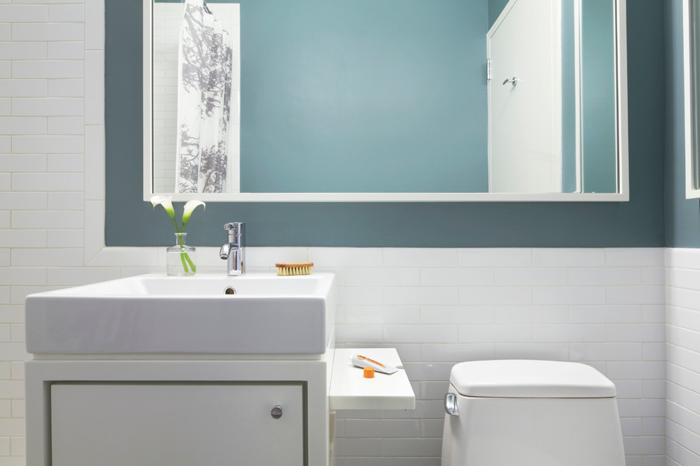 Idée de décoration pour une petite salle de bain minimaliste avec un placard à porte plane, des portes de placard blanches, un plan de toilette en surface solide, WC à poser, un carrelage blanc, des carreaux de céramique, un plan vasque, un sol en calcaire et un mur bleu.