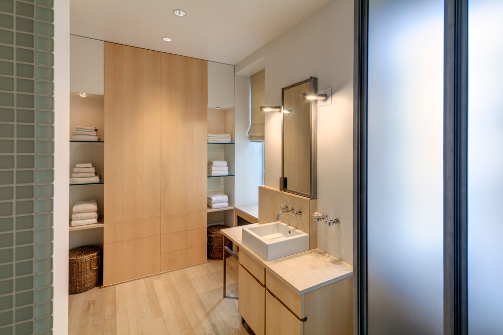Идея дизайна: главная ванная комната среднего размера в стиле модернизм с настольной раковиной, плоскими фасадами, светлыми деревянными фасадами, столешницей из известняка, открытым душем, инсталляцией, стеклянной плиткой, светлым паркетным полом и белыми стенами