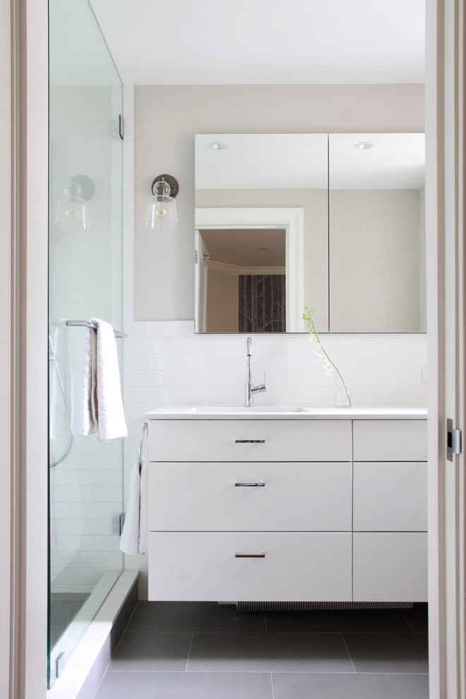 Inredning av ett modernt badrum, med vita skåp, en öppen dusch, en toalettstol med hel cisternkåpa, vit kakel, keramikplattor, vita väggar, klinkergolv i porslin, ett undermonterad handfat och bänkskiva i kvarts