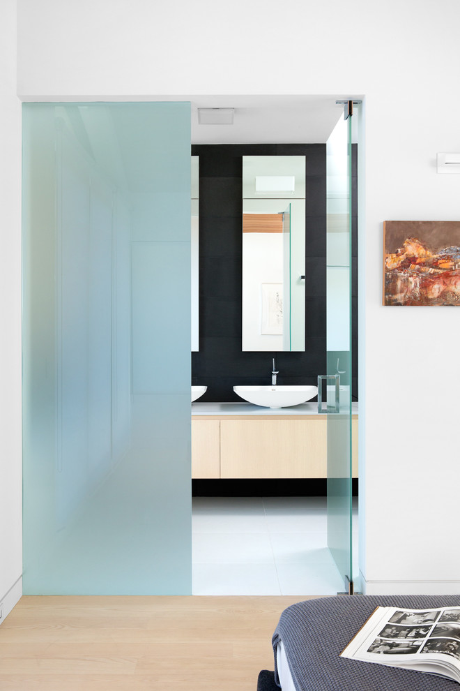 Design ideas for a small contemporary ensuite bathroom in Vancouver with a vessel sink, flat-panel cabinets, light wood cabinets, quartz worktops, a freestanding bath, a built-in shower, a wall mounted toilet, black tiles, stone tiles, white walls and porcelain flooring.