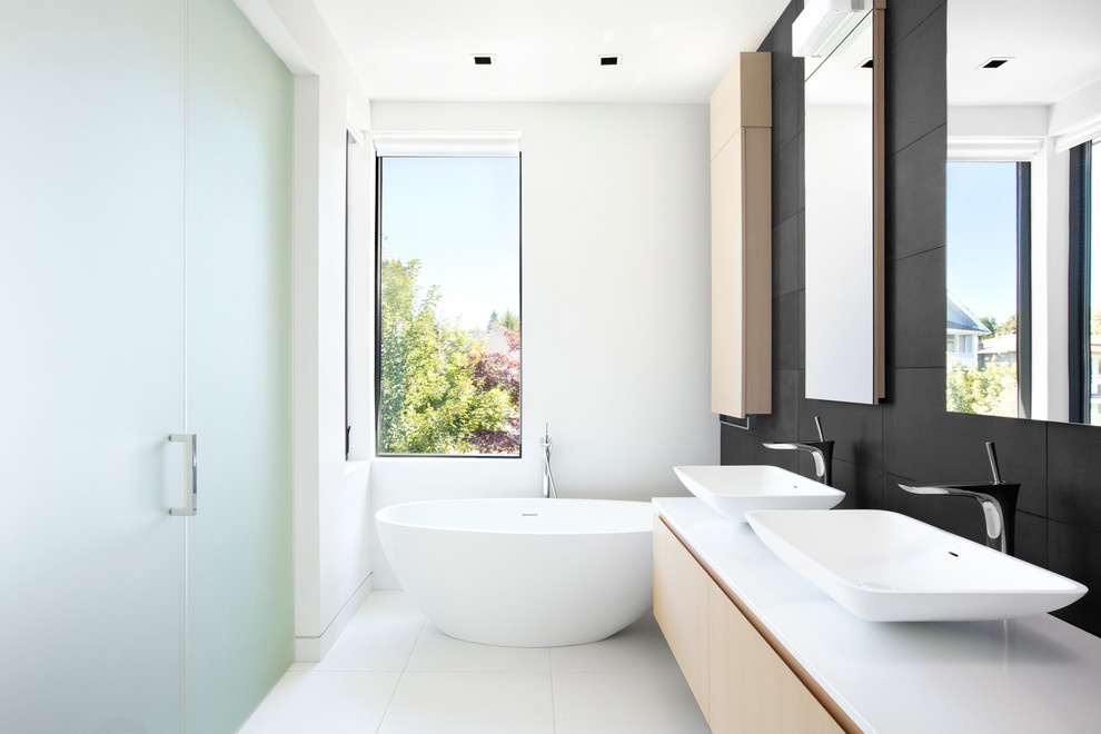 This is an example of a small contemporary ensuite bathroom in Vancouver with a vessel sink, flat-panel cabinets, light wood cabinets, quartz worktops, a freestanding bath, a built-in shower, black tiles, stone tiles, white walls and porcelain flooring.