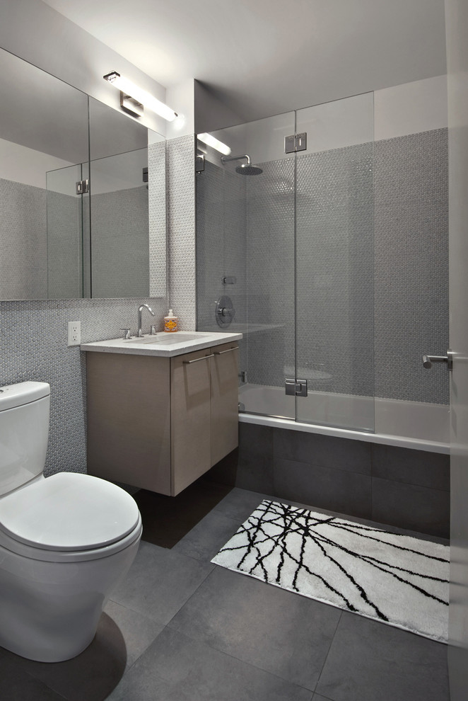 Idée de décoration pour une salle de bain design en bois clair avec une baignoire en alcôve, un carrelage gris, WC séparés, des carreaux de porcelaine, un mur gris, un sol en carrelage de porcelaine, un lavabo encastré et un plan de toilette en quartz modifié.
