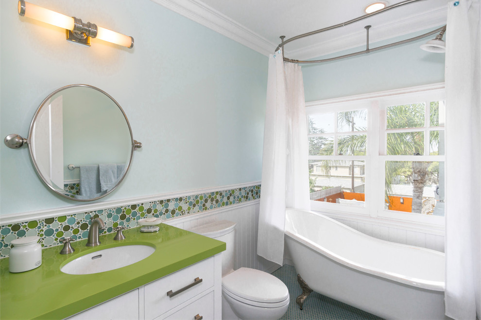 На фото: маленькая детская ванная комната в стиле неоклассика (современная классика) с фасадами островного типа, фасадами цвета дерева среднего тона, гидромассажной ванной, душем над ванной, унитазом-моноблоком, зеленой плиткой, плиткой из листового стекла, синими стенами, полом из мозаичной плитки, врезной раковиной, столешницей из искусственного кварца и синим полом для на участке и в саду