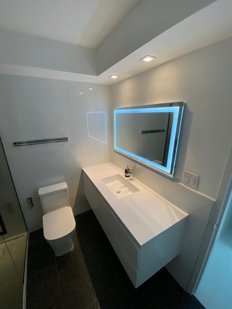 На фото: маленькая ванная комната в стиле модернизм с плоскими фасадами, белыми фасадами, открытым душем, унитазом-моноблоком, белой плиткой, керамической плиткой, белыми стенами, полом из керамической плитки, душевой кабиной, накладной раковиной, столешницей из искусственного кварца, черным полом, душем с раздвижными дверями, белой столешницей, тумбой под одну раковину и подвесной тумбой для на участке и в саду с