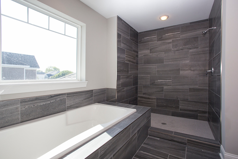 Cette image montre une grande douche en alcôve principale design avec une baignoire posée, un carrelage gris, des carreaux de porcelaine, un mur beige, un sol en carrelage de porcelaine et un sol gris.
