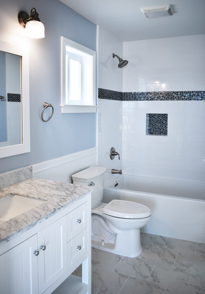 Maritim inredning av ett mellanstort badrum med dusch, med möbel-liknande, vita skåp, ett badkar i en alkov, en dusch i en alkov, en toalettstol med separat cisternkåpa, vit kakel, keramikplattor, blå väggar, klinkergolv i porslin, ett undermonterad handfat, marmorbänkskiva, grått golv och dusch med duschdraperi