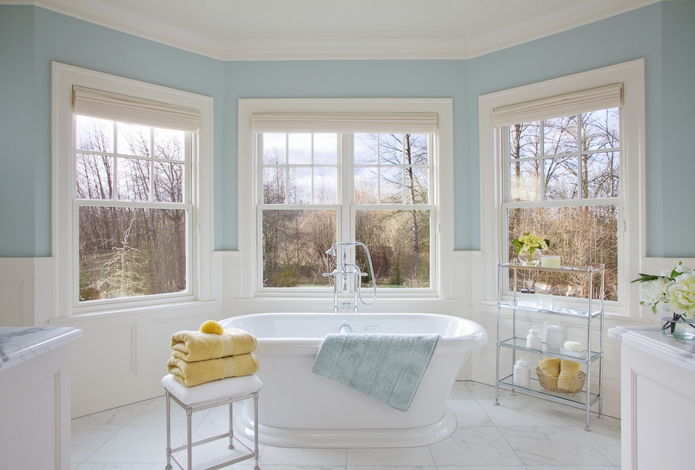 На фото: большая главная ванная комната в классическом стиле с отдельно стоящей ванной, белой плиткой, фасадами с утопленной филенкой, синими стенами, полом из керамогранита, мраморной столешницей и окном с