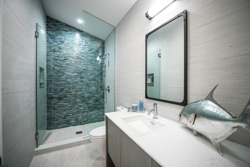 Exemple d'une douche en alcôve principale exotique en bois foncé de taille moyenne avec un placard à porte plane, WC à poser, un carrelage bleu, un mur gris, un lavabo encastré et une cabine de douche à porte battante.