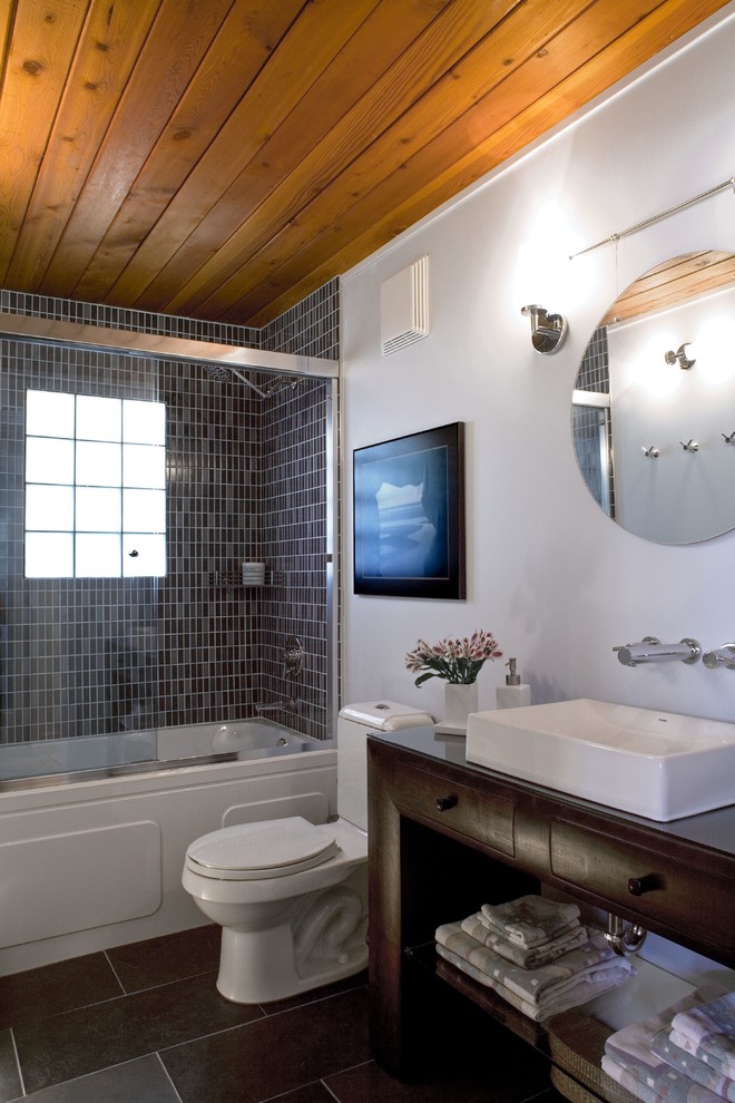 Cette image montre une salle d'eau design en bois foncé de taille moyenne avec une vasque, un placard en trompe-l'oeil, un plan de toilette en bois, un combiné douche/baignoire, WC séparés, un carrelage bleu, un carrelage de pierre, un mur blanc, un sol en ardoise et un sol gris.
