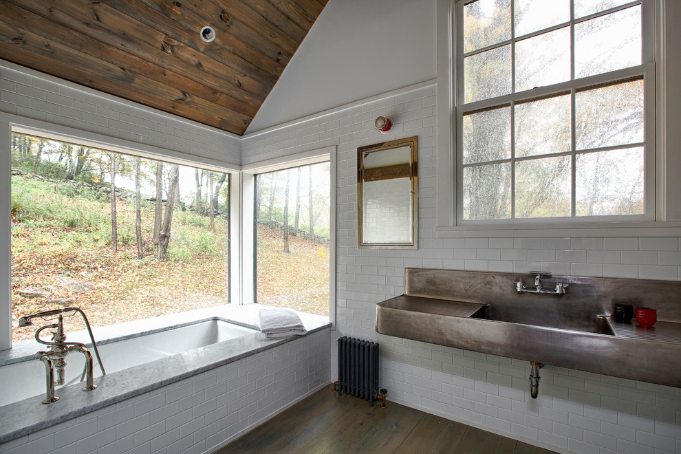 Cette image montre une salle de bain rustique avec une baignoire encastrée, un carrelage blanc, un carrelage métro, un mur blanc, un sol en bois brun, un lavabo intégré, un sol marron et un plan de toilette gris.