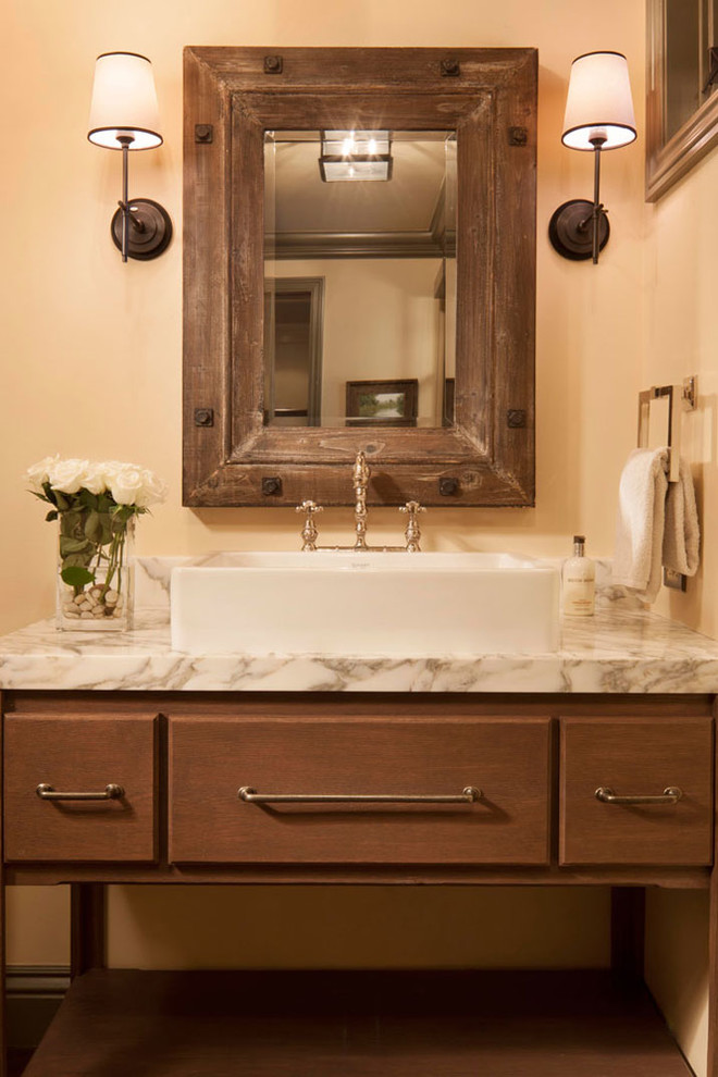 Foto de cuarto de baño rectangular clásico con lavabo sobreencimera, puertas de armario de madera en tonos medios, paredes beige, suelo de madera oscura y armarios con paneles lisos