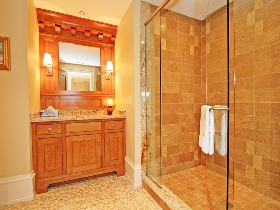 Modelo de cuarto de baño clásico con lavabo bajoencimera, puertas de armario de madera oscura, encimera de mármol, ducha empotrada, baldosas y/o azulejos marrones y baldosas y/o azulejos de piedra