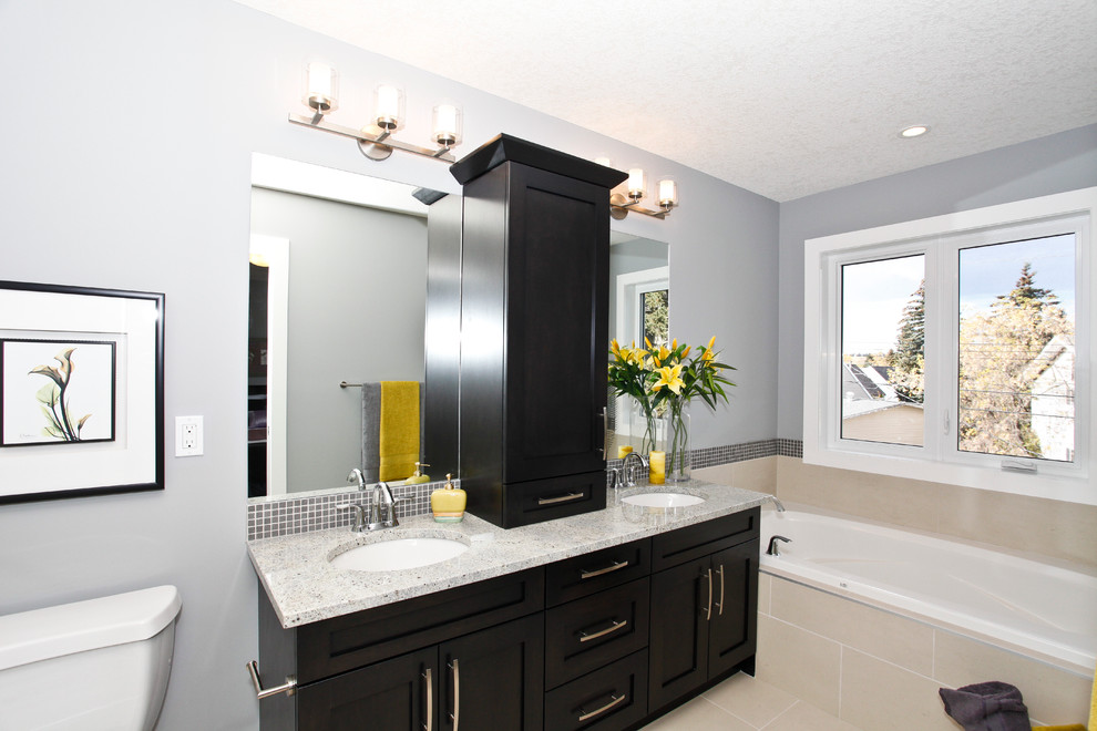 Example of a mid-sized transitional master beige tile and stone tile porcelain tile bathroom design in Calgary with shaker cabinets, blue cabinets, gray walls, an undermount sink, granite countertops and a two-piece toilet